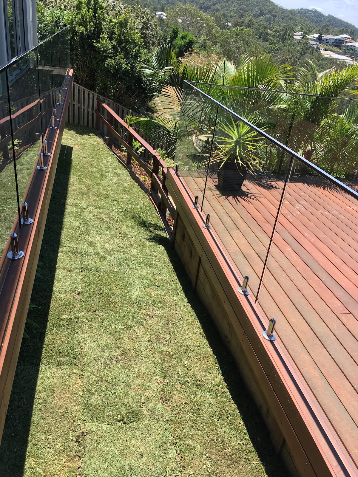 Fresh strip of lawn between a timber deck with glass balustrade and a retaining wall