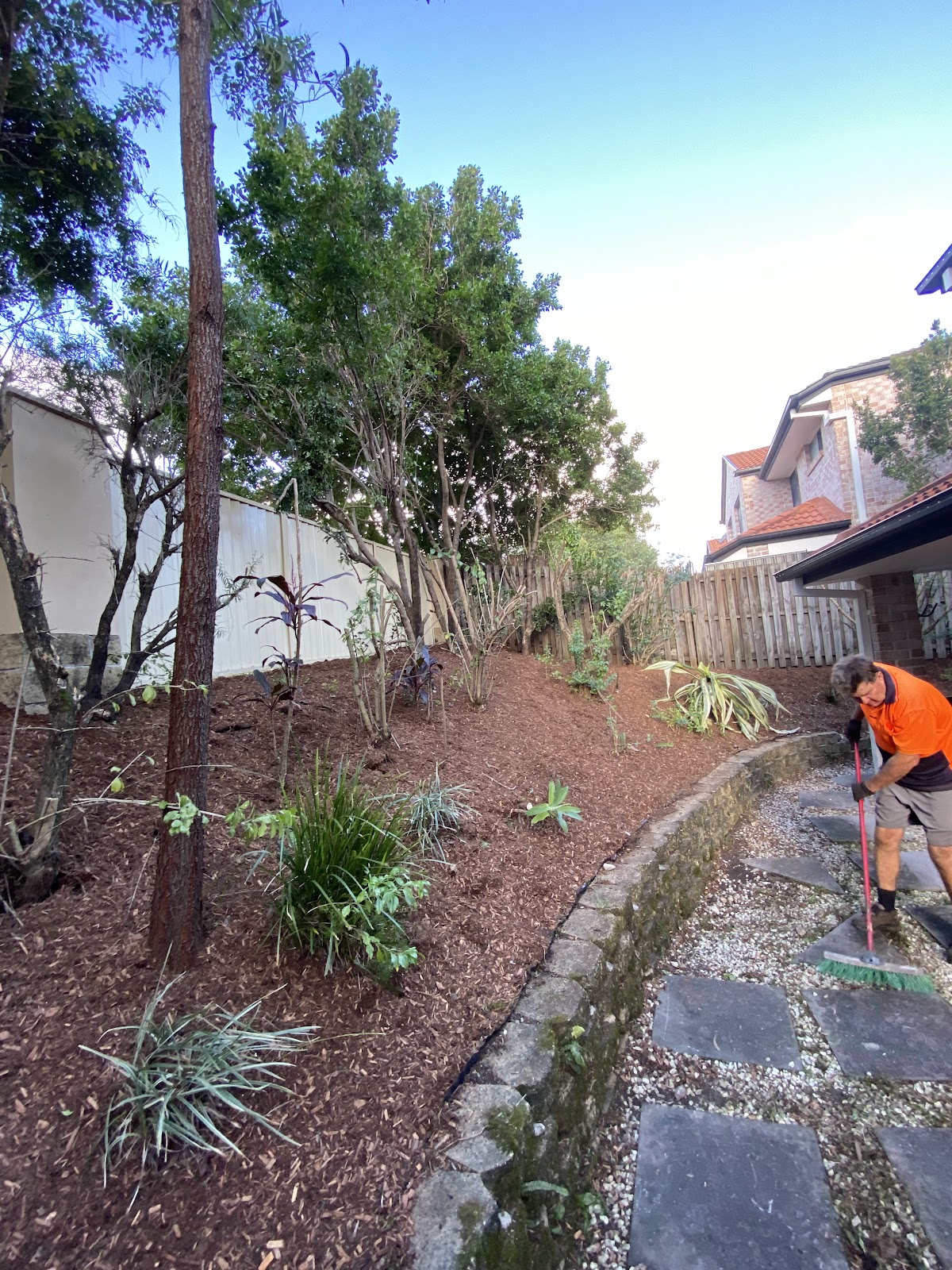 Team member in hi-vis sweeping the path after mulching and planting a garden bed